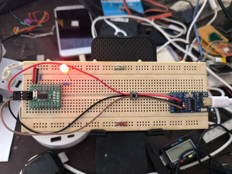 A CH32V003 breakout board on a breadboard with a lit LED and current-limiting resistor, wired by three jumpers to the blue WCH-Link clone on the right, USB-C cable running off frame